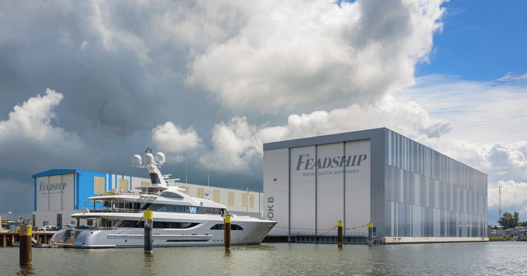 Feadship superyacht W anchored outside Feadship shipbuilding facility, surrounded by water