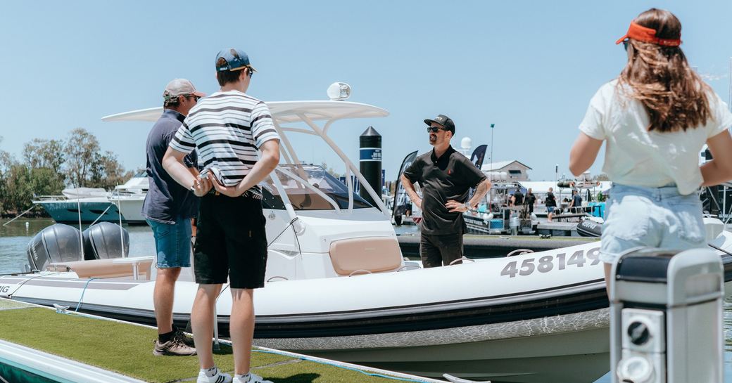 Representative in fishing boat talking to visitors on the dock at Sanctuary Cove Boat Show.