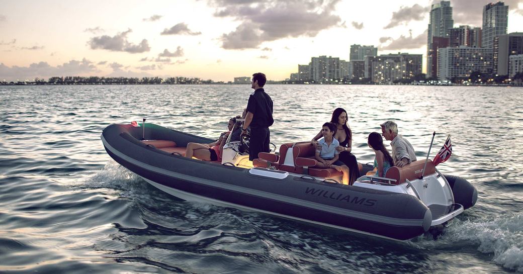 Family of four, including two children, on tender boat with man at helm driving and large buildings on coastline in background