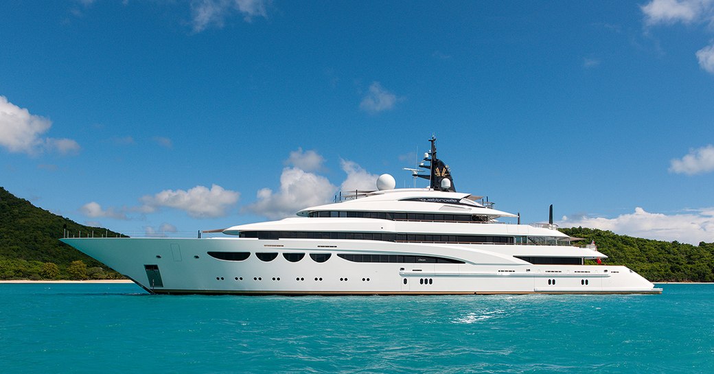 Superyacht QUATTROELLE underway, with azure waters and an island in background. 