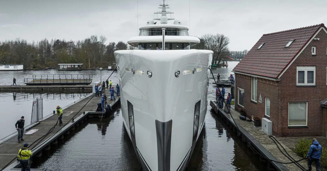 Frontal view of the bow on Feadship Project 823, surrounded by building facility and green foliage in the background.