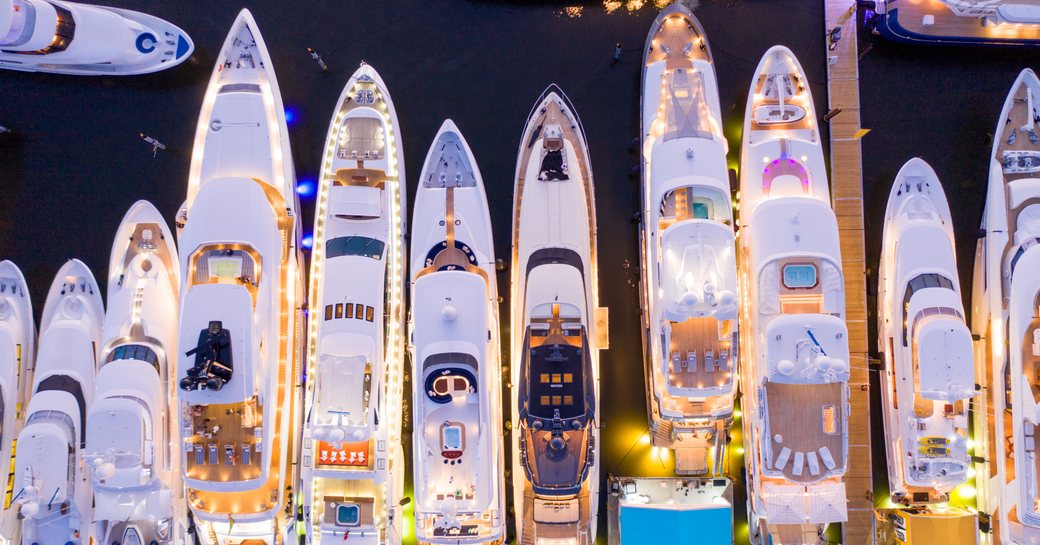 Line up of superyachts moored at night, aerial view overlooking lit up superyachts surrounded by sea