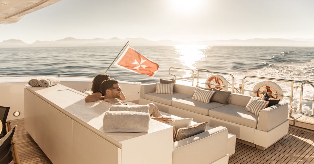 Young couple sitting on comfortable sofa at back of yacht in beautiful sunlight looking across the sea