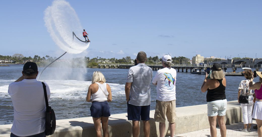 Watersports demonstrator performing flyboarding at the Palm Beach International Boat Show, with show visitors watching from the dockside