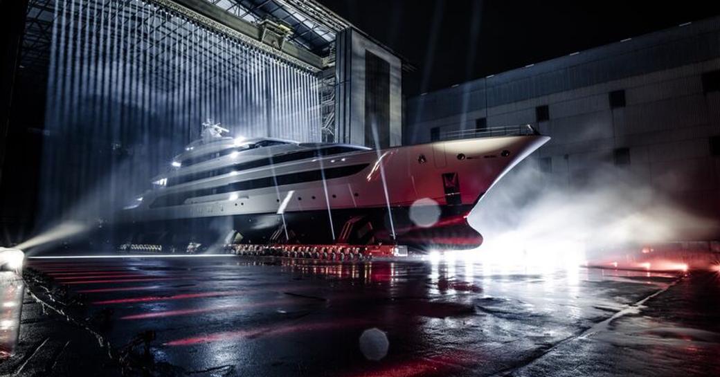 Oceanco superyacht H emerging from shed with beams of light shining on the hull.