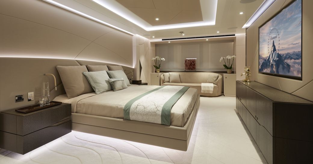 Master cabin onboard Heesen 'Project Triton', central berth to port side facing mounted flatscreen TV, with sofa in background