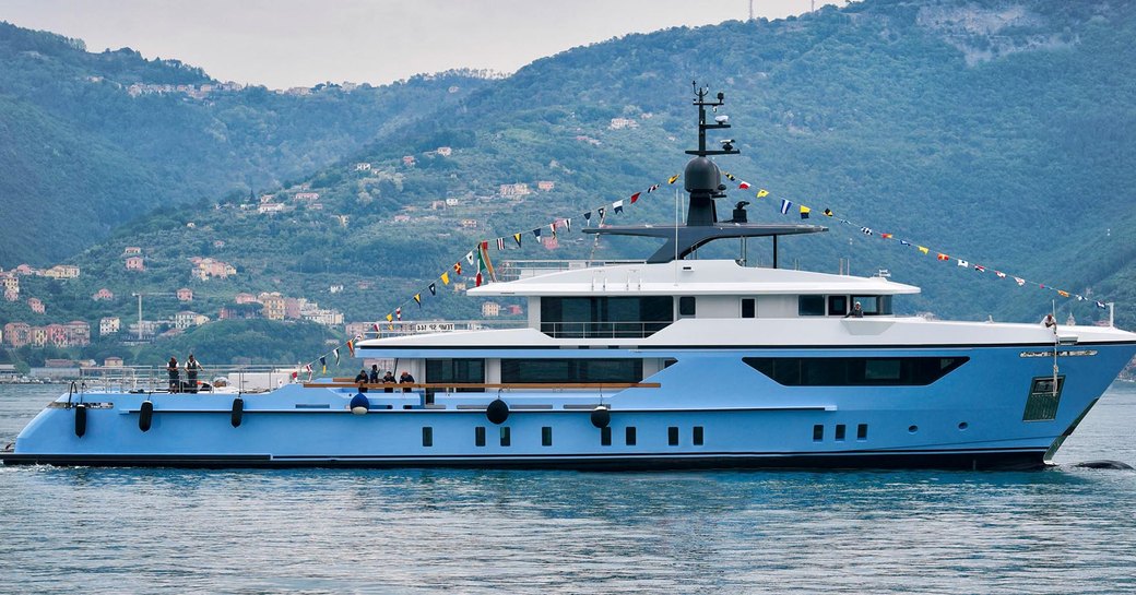 Side view of Sanlorenzo 500EXP underway at launch, adorned with flags and Italian hillside in background.