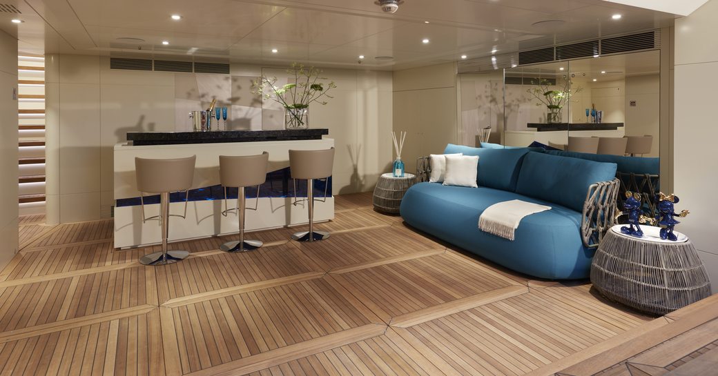 Beach club onboard Heesen 'Project Triton', wet bar in background with teal sofa to starboard