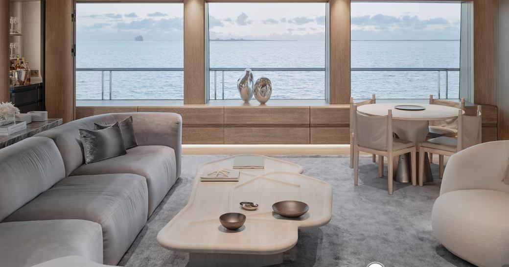 Overview of the main salon onboard superyacht ENTOURAGE. Long sofa to port side with extensive glazing in background and a small circular table with chairs.