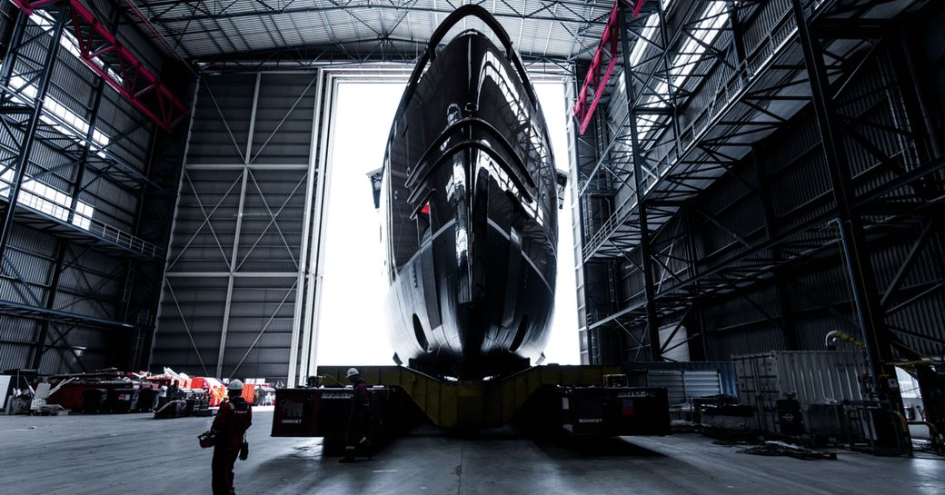 Hull of Damen Yachting's 'La Datcha' Explorer Yacht in front of open warehouse door with person in foreground