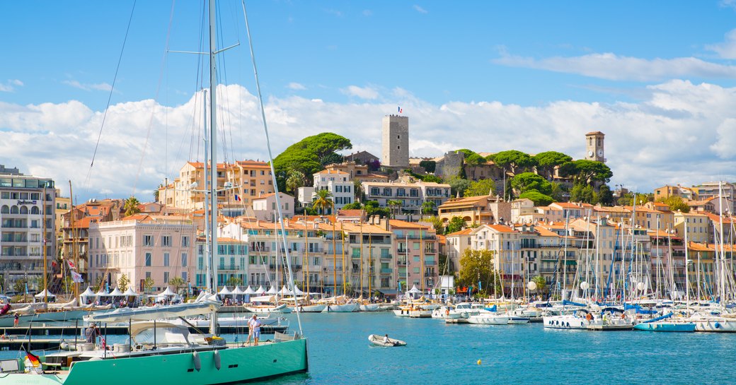 Overview of Cannes Vieux Port, sailing boats and motor yachts berthed in marina, overlooking Cannes in background.