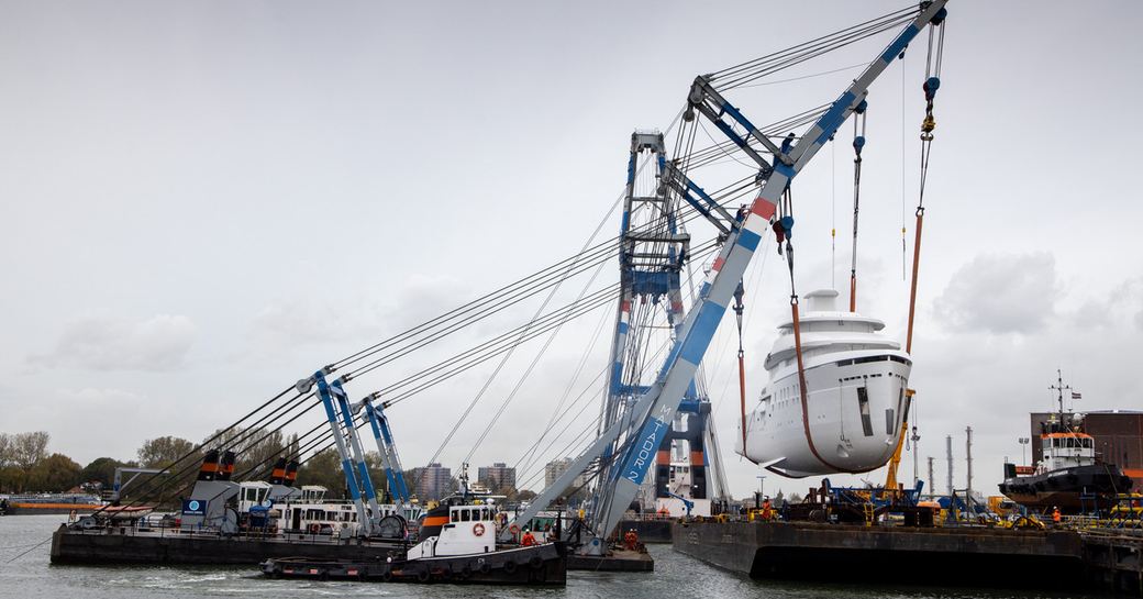 Feadship explorer yacht SHINKAI being airlifted by crane, surrounded by river and shipyard facility