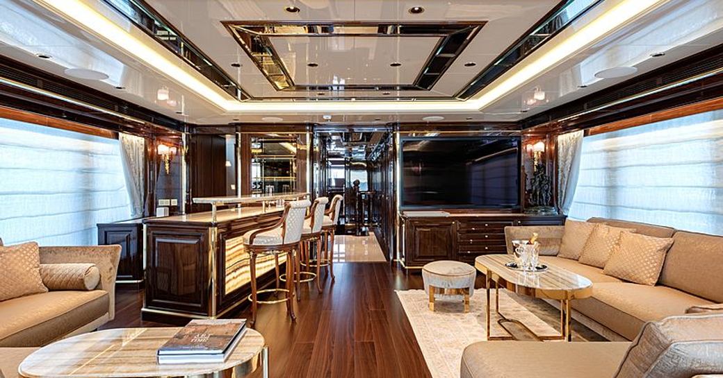 Long view of main salon onboard Sanlorenzo Lady Lena, sofas on either side with adjacent coffee tables, bar and stools in background