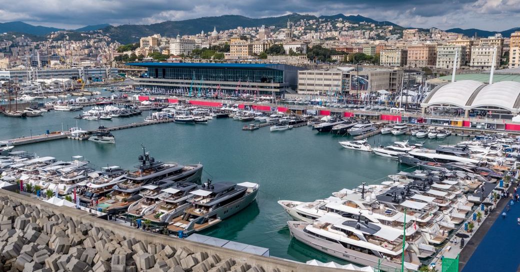 Overview of Genoa International Boat Show, many motor yachts berthed around dockside with exhibitor stands in distance.