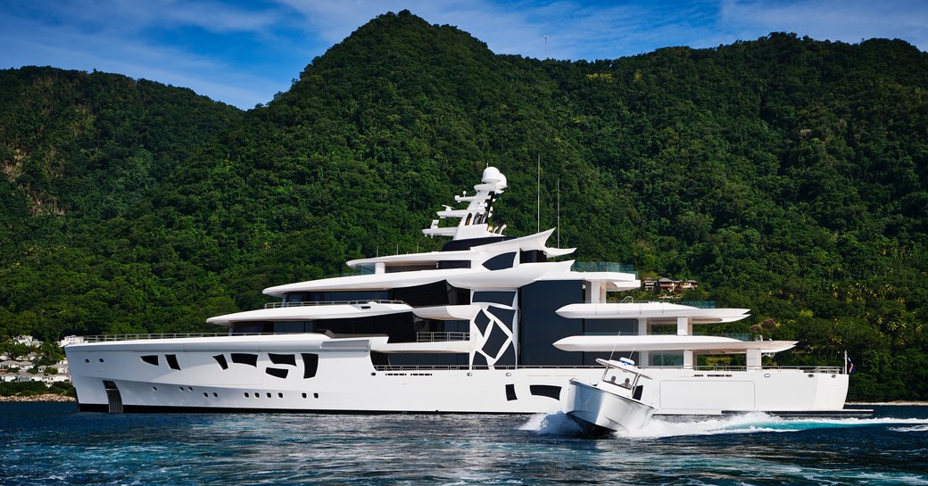 Superyacht ARTEFACT at anchor with tender speeding away. Elevated terrain in background.