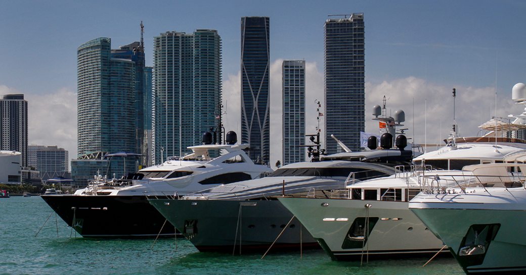 Superyachts moored at Miami Yacht Show, skyscrapers in background.