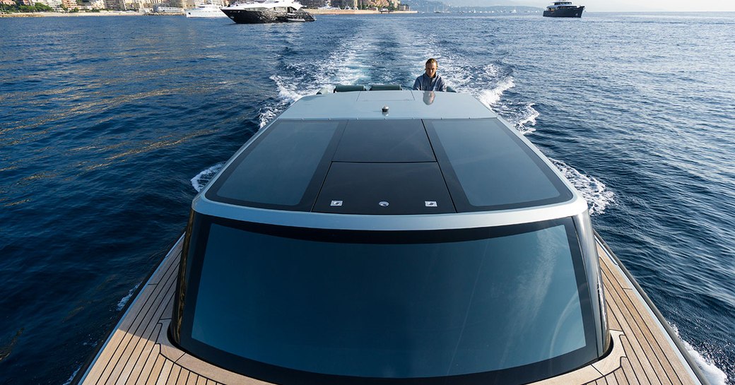 View of limousine tender from front with wood decking and glass exterior and man driving with coastline in background