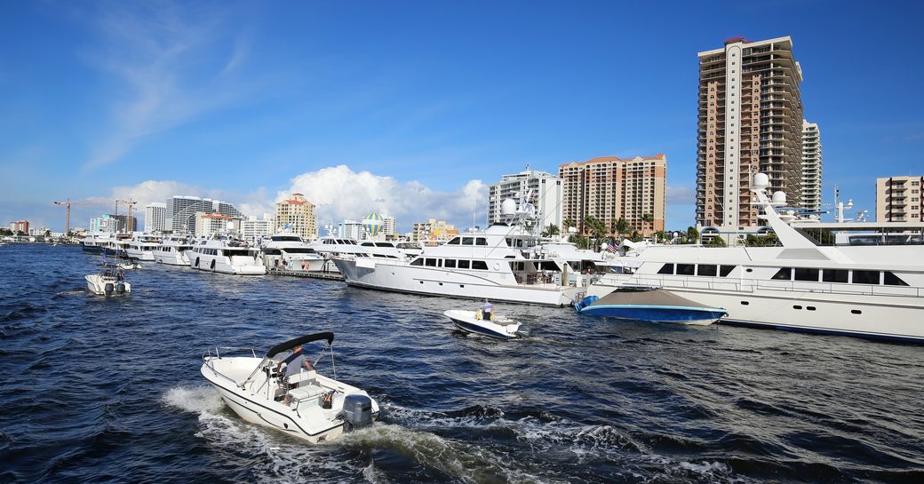 Superyachts at anchor at FLIBS with Fort Lauderdale in background and a passing boat in foreground