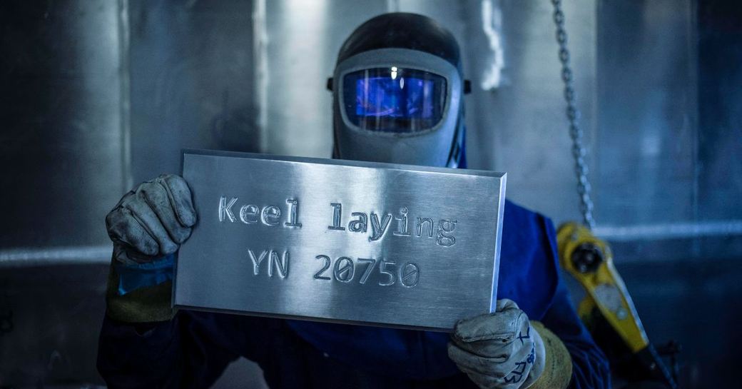 Shipbuilder holding up plaque reading 'Keel laying YN 20750'.