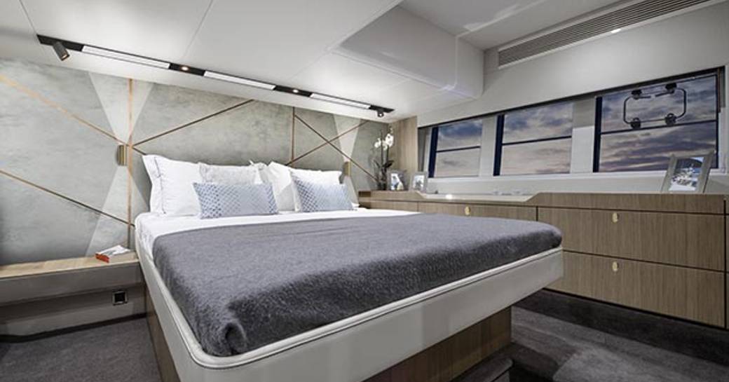 double bed with white and grey linen, grey carpets, white wall panels and wooden storage in the master suite on board the Squadron 50