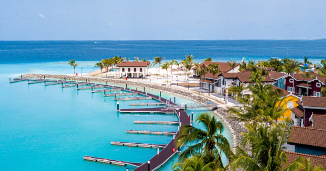 Side angle view of facilities at Crossroads Maldives Marina, range of buildings accompanied by semi circle of empty marina berths, with sea in background