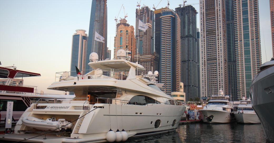 Superyachts moored at Dubai International Boat Show, aft view of a superyacht in foreground with others facing. Skyscrapers across background.