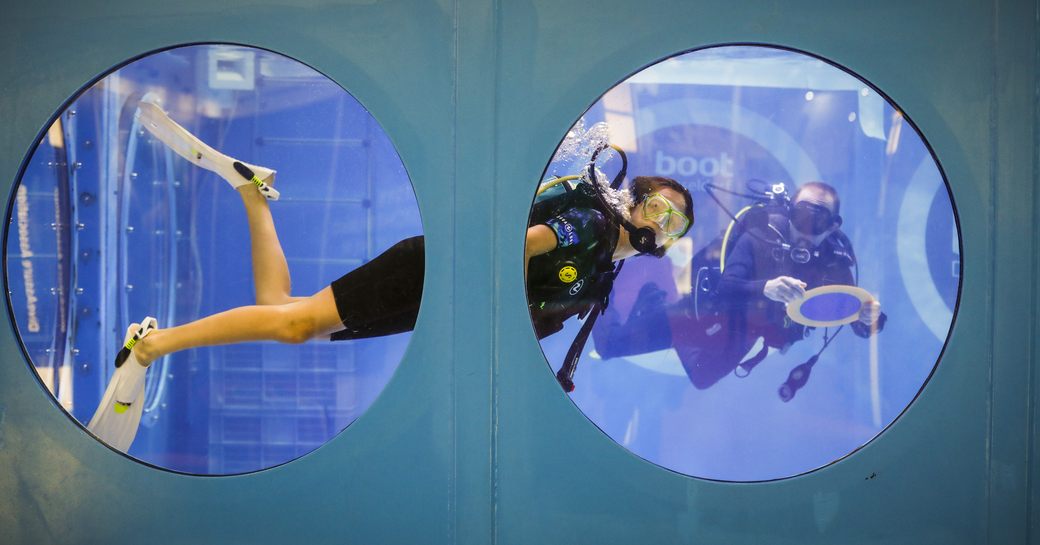 Diving demonstration at boot Dusseldorf show. Female diver visible in large tank through two adjacent circular windows.