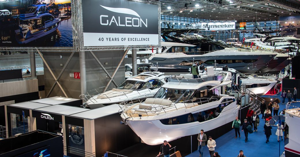 Overview of Galeon stand boot Dusseldorf, motoryachts on display with visitors walking around on blue carpet.