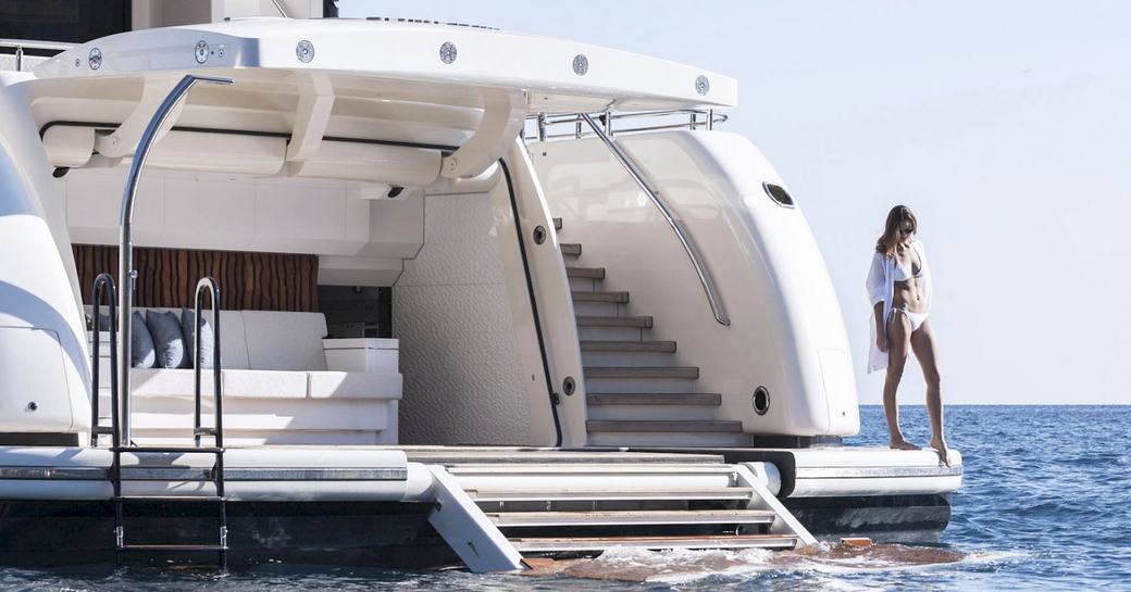 Young female standing on edge of yacht, about to dip her toe into water