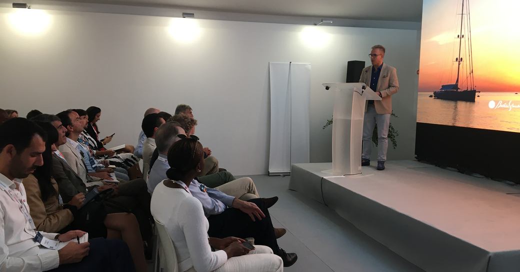 Side view of the Sustainability Conference at the Monaco Yacht Show. Speaker at podium talking to small seated audience.