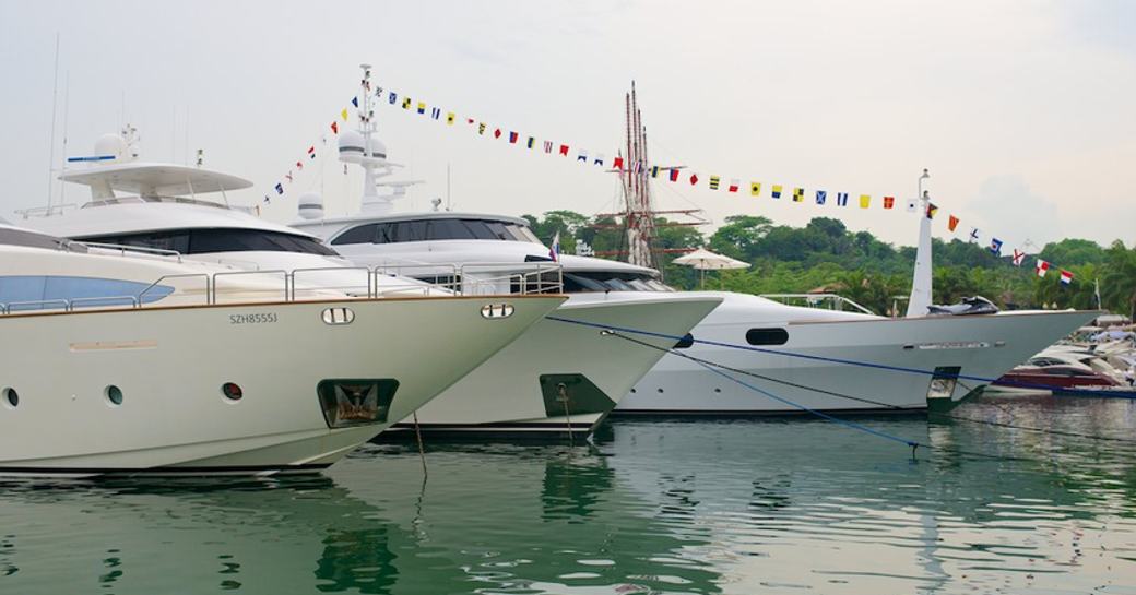 Three motor yachts moored at Singapore Yacht Show with flag decorations. 