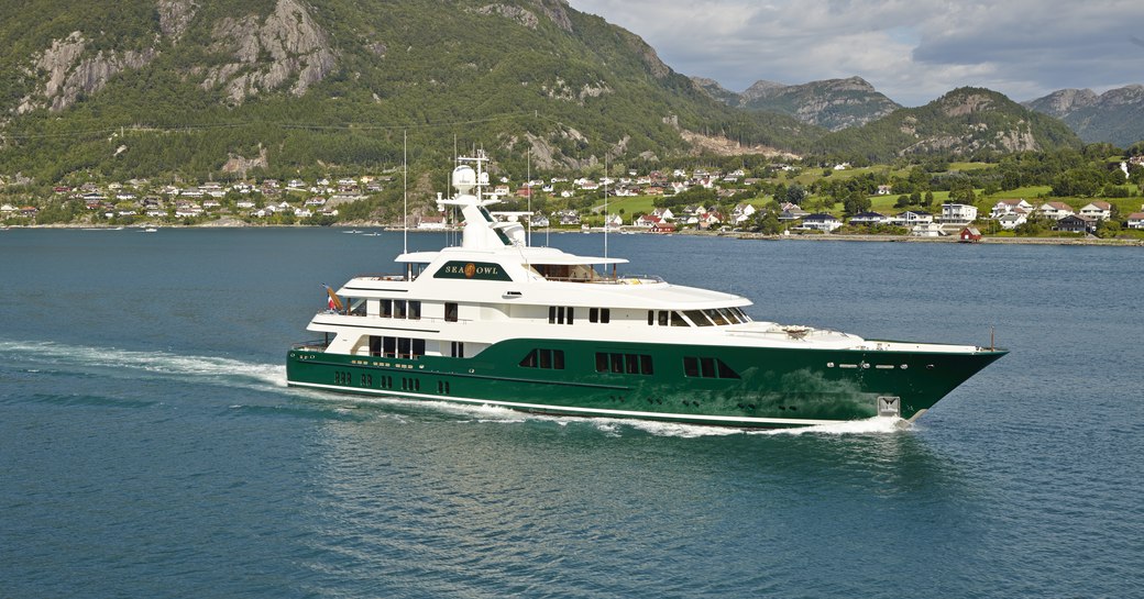 Superyacht Sea Owl underway, surrounded by sea and mountains in background.