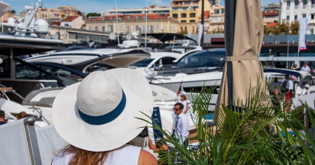 A female visitor to the Cannes Yachting Festival looks out over the marina, with Cannes town visible in background.