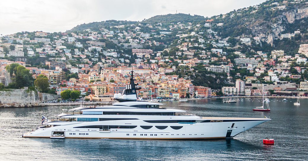 Side view of megayacht AHPO underway with residential settlement in background.