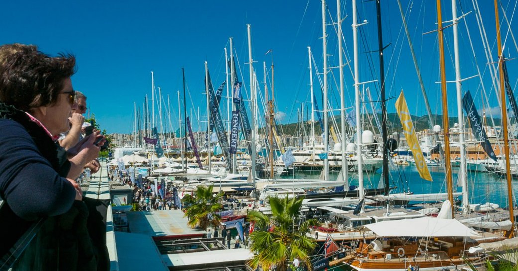 Visitors looking over balcony at Palma Superyacht Show, many sailing boats berthed in front.