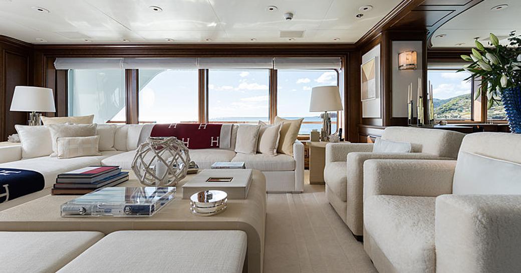 Main salon onboard Feadship superyacht FLAG, overview of white seating surrounding coffee table with wide stretch of glazing in background.