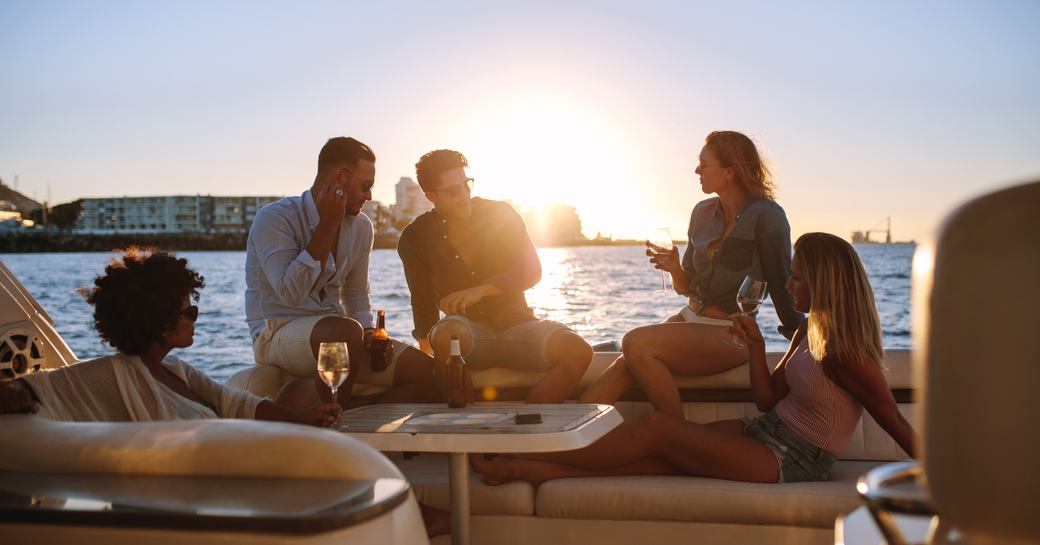 Young rich friends drinking wine and beers in boat party during sunset. Group of young people partying on yacht.