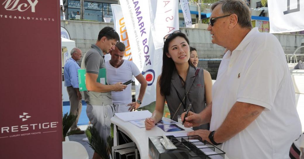 Male and female visitor to Thailand Yacht Show talking at a shipyard exhibit stand during show.