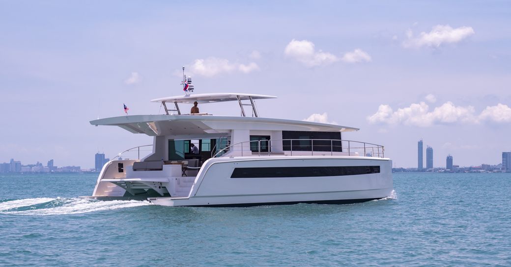 Aft angle view of Silent 60 catamaran underway, surrounded by sea with cosmopolitan skyscrapers on distant horizon.