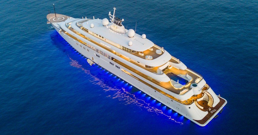 Lurssen yacht GOLDEN ODYSSEY shown in aerial shot over port aft and side profile; yacht is underway but not making way, in low lighting as the underwater lines are on