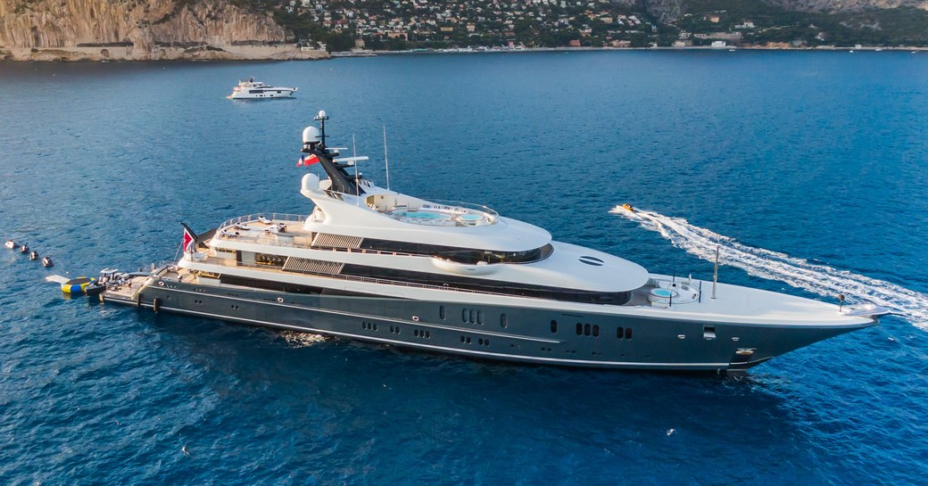 Lurssen yacht PHOENIX 2 aerial view over starboard bow and side profile whilst yacht still in calm waters, land in background, watercraft creating wash in backgrounf