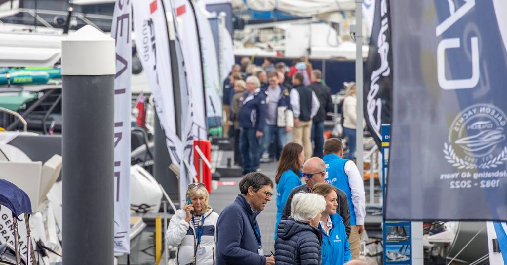 A busy pontoon with visitors and brand representatives with yachts for sale on either side