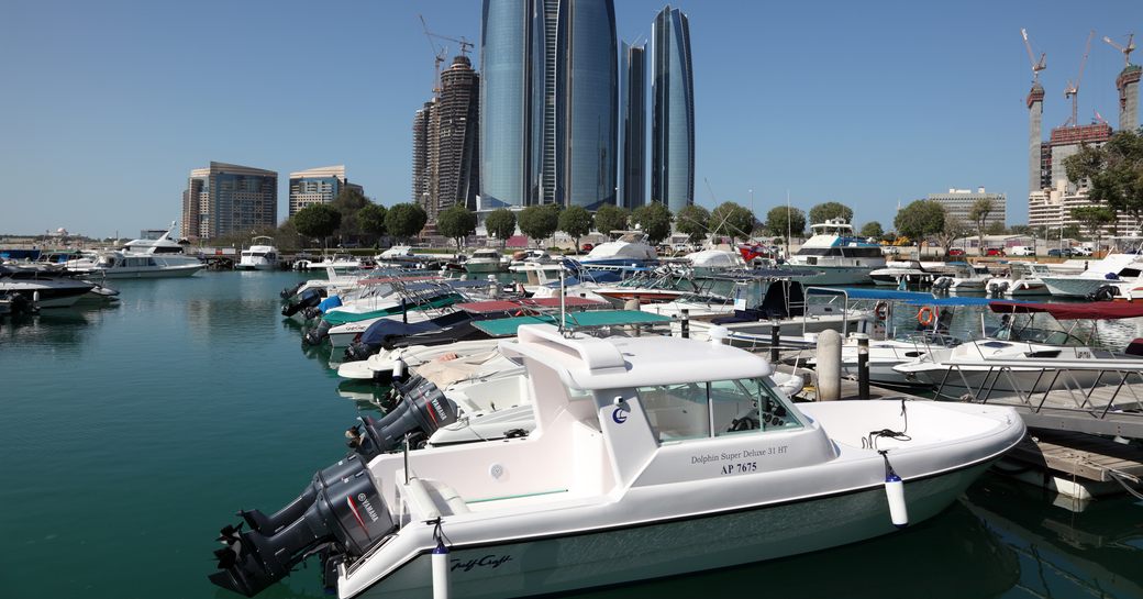 Overview of a marina in Abu Dhabi at water level, with boats berthed along pontoons and skyscrapers in the background