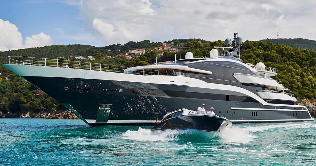 Oceanco yacht DAR shown on anchor from water level towards port bow and side profile, with tender moving in foreground and land in background