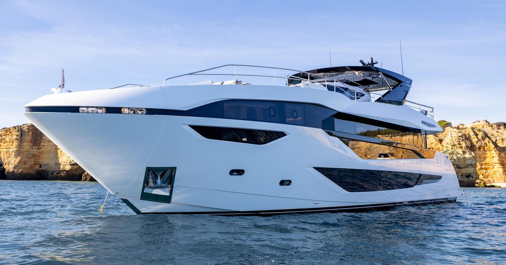 Overview of Sunseeker 100 Yacht at anchor in a bay, with cliff in the background.