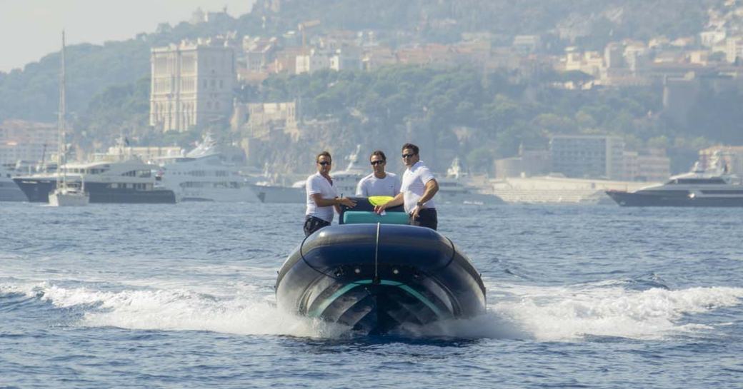 Three males on SOLAS tender with rugged coast in background