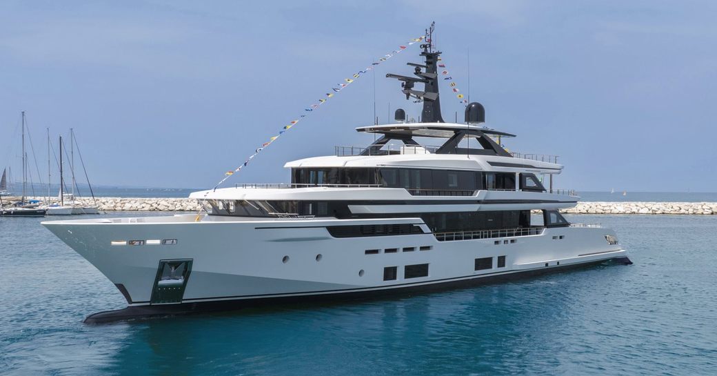 Custom Line 50 M/Y ASANTE shown port bow and alongside port side profile making way slowly in calm waters on bright day, marina with sailing yachts in background as can see masts