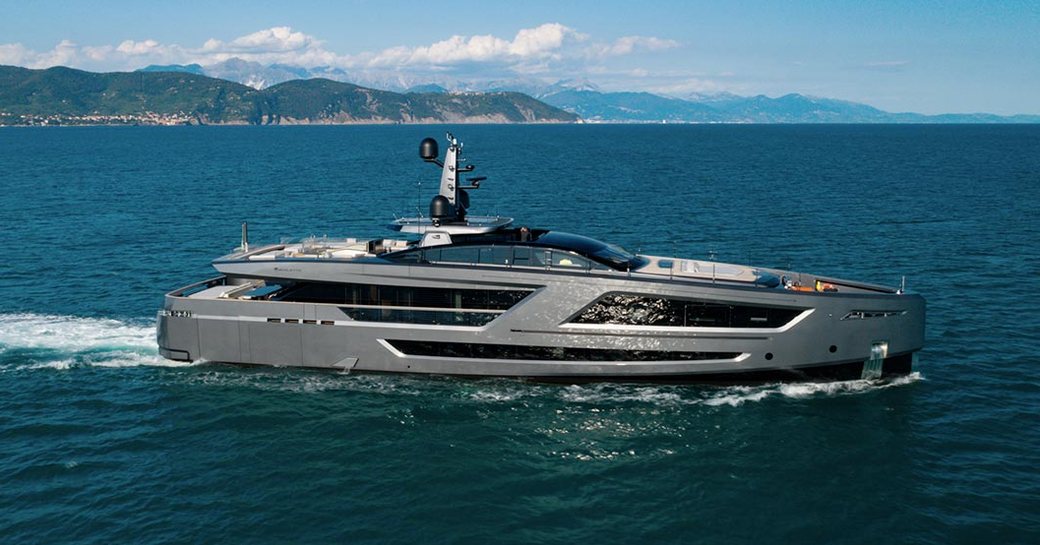 Superyacht PANAM underway, surrounded by sea with elevated terrain on left hand side.