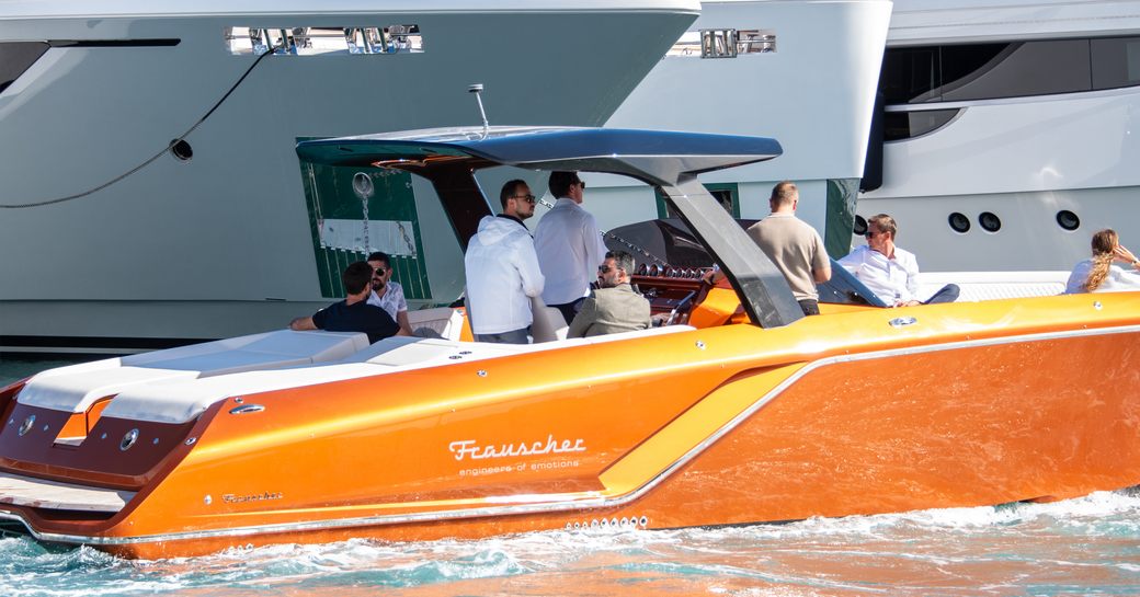 golden colour limousine yacht tender transporting a few VIP guests at Cannes Yachting Festival 2024, boat making it's way down the marina channel past the bow of superyachts