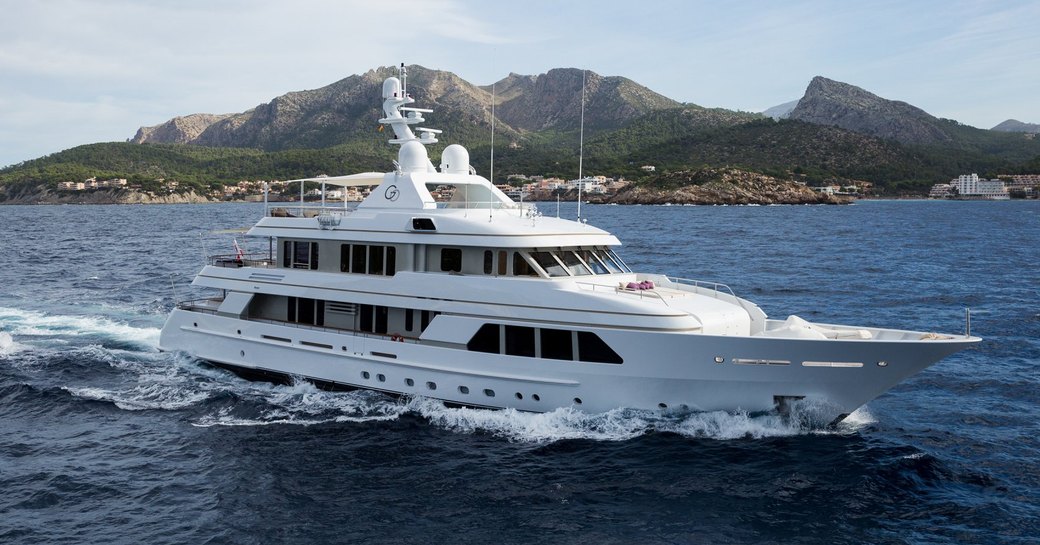 Feadship yacht GO shown in running shot in calm sea on clear day with land in background, yacht is shown starboard bow and side profile